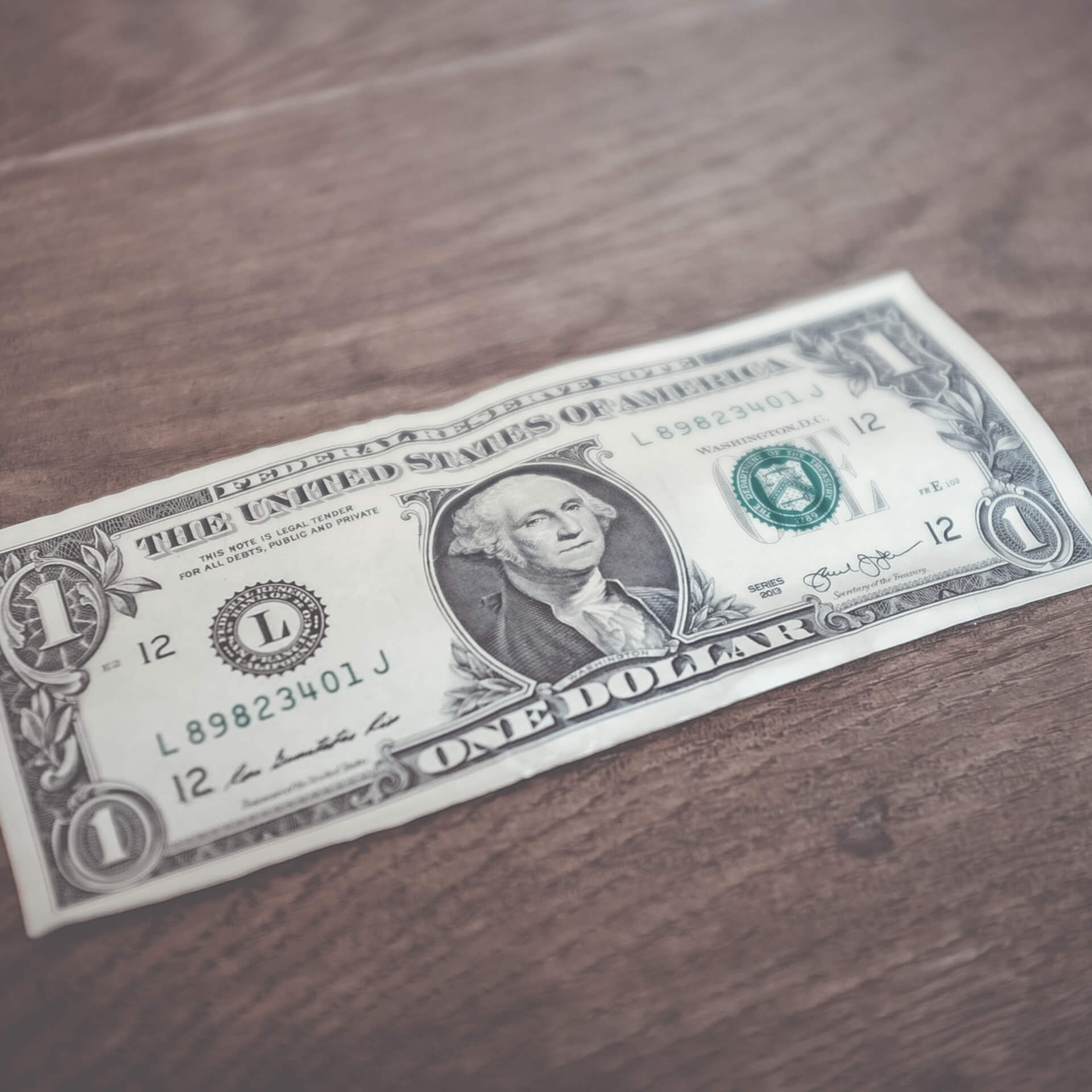 reacting nonprofit donors: One dollar bill face up on a brown wooden table.